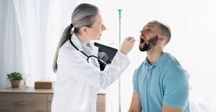 Doctor examining a patient's throat with a tongue depressor in a well-lit medical office.